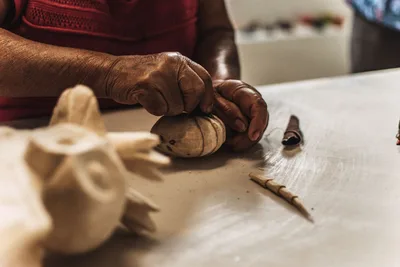 Primer plano detallado de manos esculpiendo madera en una escultura, mostrando la destreza artesanal tradicional.